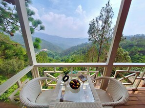 Un balcón con sillas de mimbre y una mesa, con vistas a un paisaje montañoso.