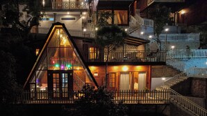 A multi-story building with a prominent triangular glass structure at the front, wooden balconies, and a staircase leading to the upper levels. - Koro Treehouse Resort (Solan)