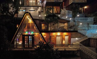 A multi-story building with a prominent triangular glass structure at the front, wooden balconies, and a staircase leading to the upper levels.