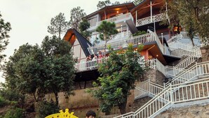 A playground with a slide and climbing structure, surrounded by a stone wall and trees. - Koro Treehouse Resort (Solan)