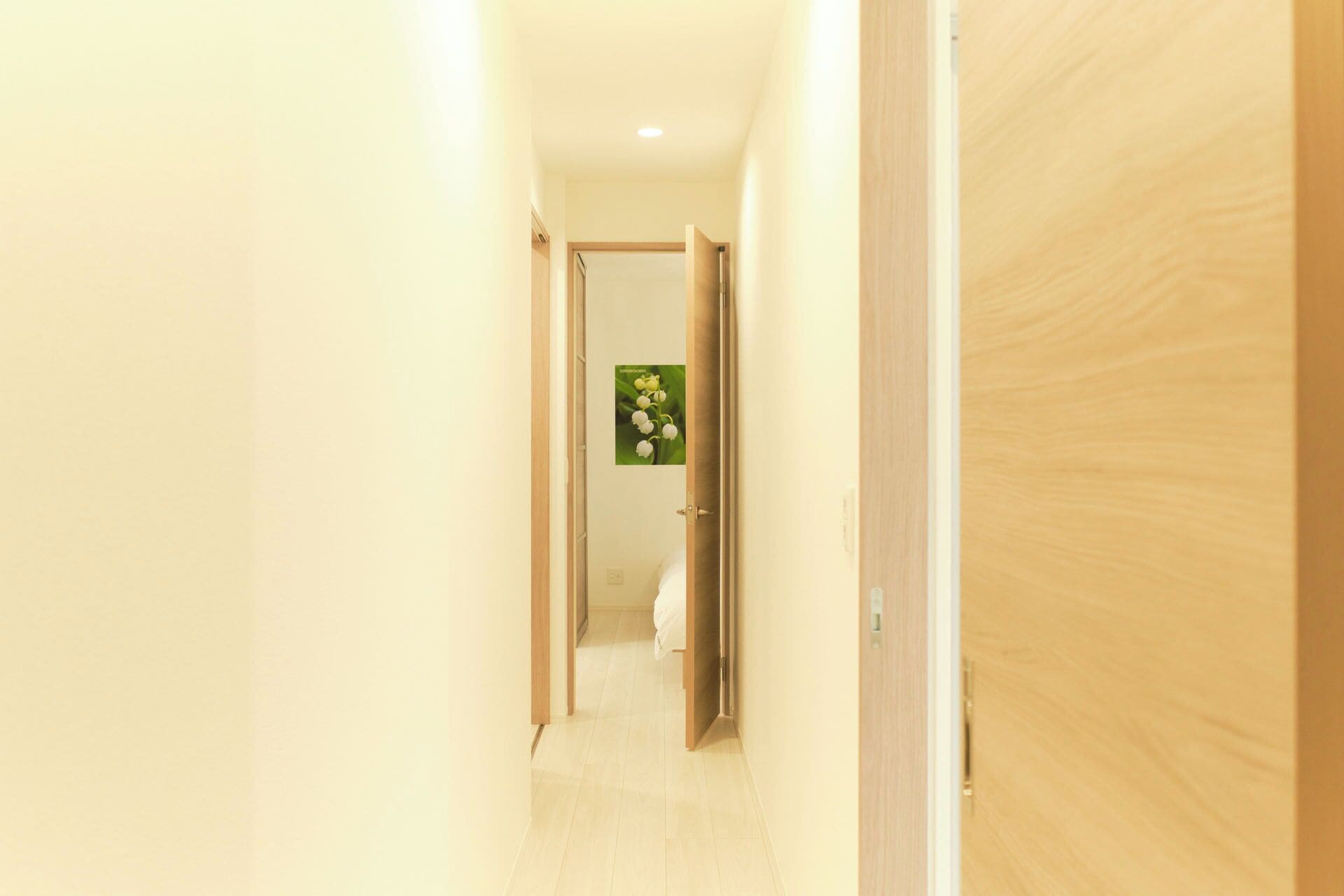 A hallway with a wooden door on the right, a white wall, and a door at the end with a green floral decoration.