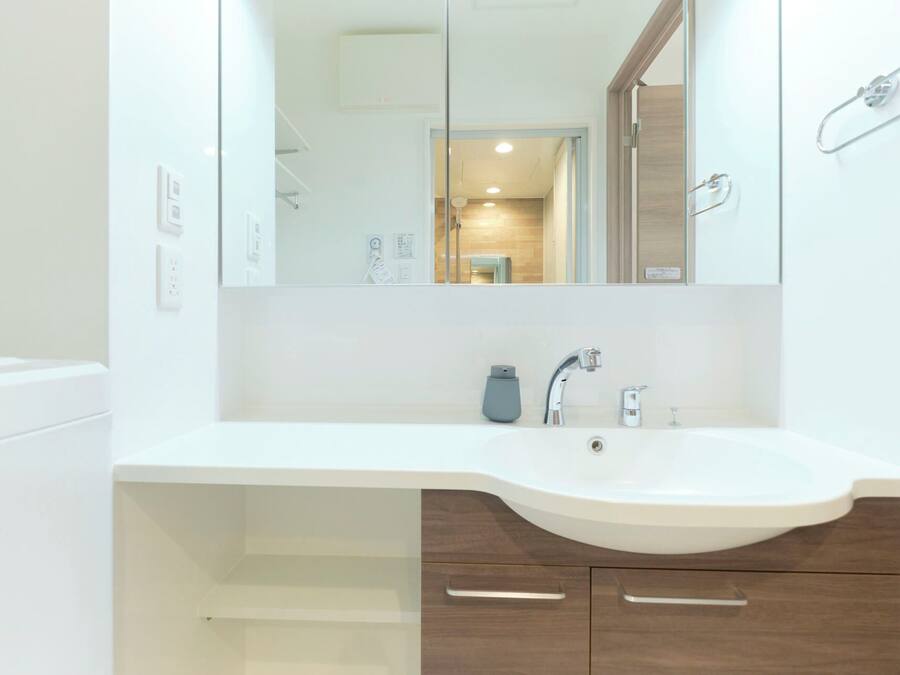A modern bathroom with a white sink, a mirror, and wooden cabinets.