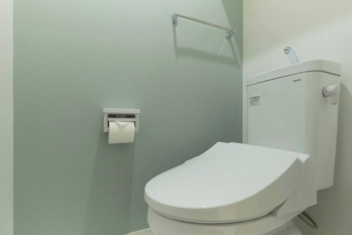 A bathroom with a white toilet, a paper towel dispenser, and a toilet paper holder on the wall.