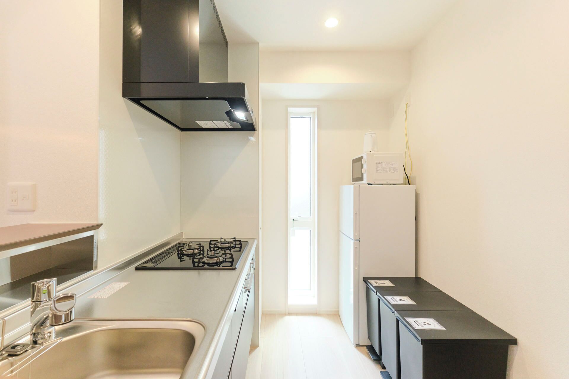 A narrow kitchen with a gas stove, a sink, and a microwave. There is a door leading to another room.