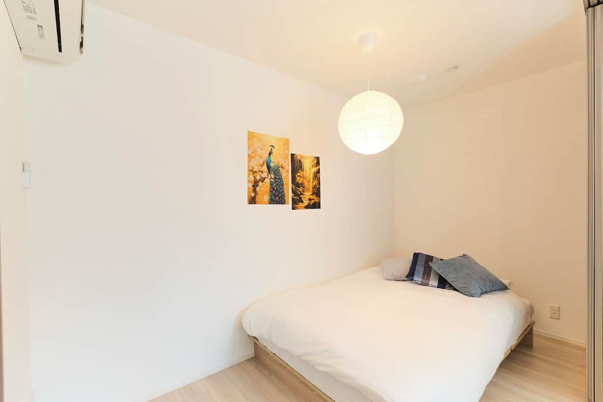 A bedroom with a bed, a hanging light fixture, and two wall-mounted pictures.