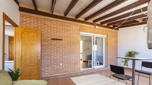 A patio area with a brick wall, a sliding glass door leading to an interior room, a small table with chairs, and a green sofa. - Ático Playa Zapillo by Interhome (Almería)