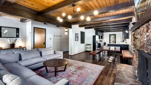 A modern living room with a wooden ceiling, a large sofa, a coffee table, and a fireplace. - Modern Retro Tahoe Chic Chalet (Tahoe City)