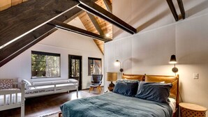 A bedroom with a loft-style ceiling, a bed with a headboard, a chair, a bedside table, and a lamp. - Modern Retro Tahoe Chic Chalet (Tahoe City)