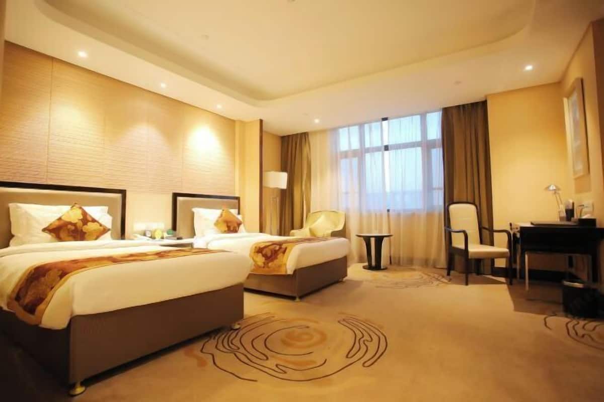 Habitació d'hotel amb dos llits, una taula de treball, una cadira i un finestral gran.