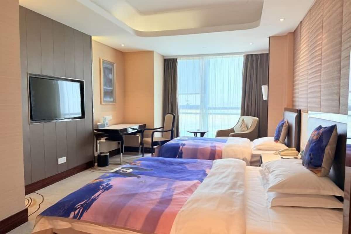 Habitació d'hotel amb dos llits, una taula de treball, una cadira, un televisor i una finestra amb cortines.