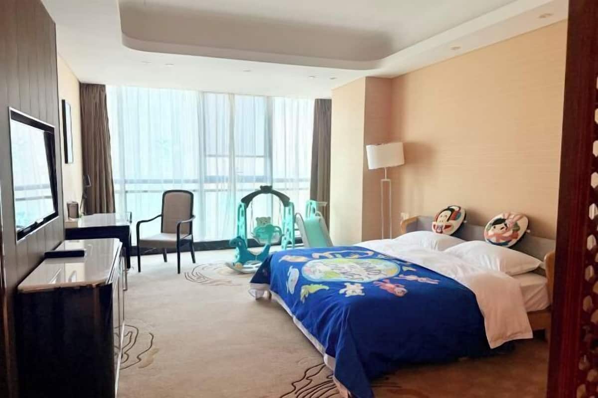 Habitació d'hotel amb llit, escriptori, cadira, televisió i finestra amb cortines.