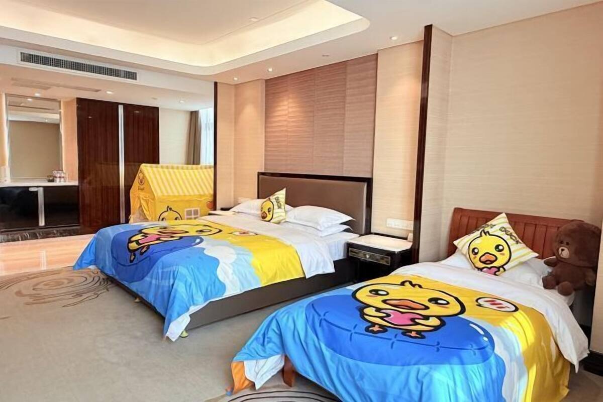 Habitació d'hotel amb dos llits, cadascun amb roba de llit de temàtica de dibuixos animats, un gran os de peluix i un disseny modern.