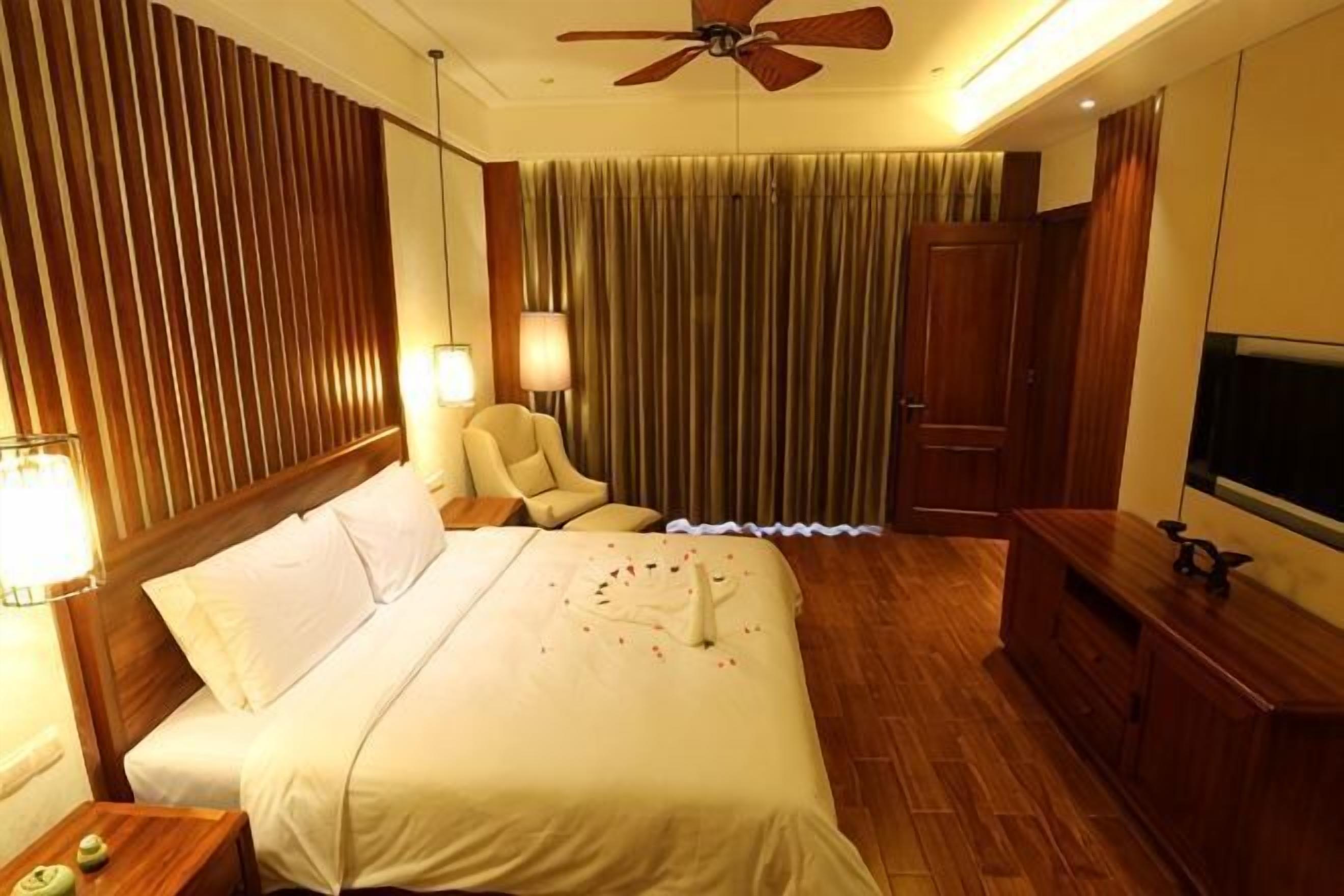 A hotel room with a bed, a chair, a desk, a TV, and a ceiling fan.