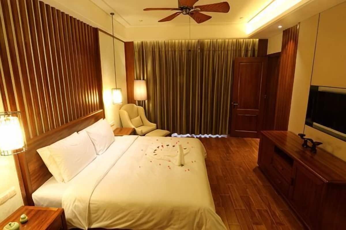 A hotel room with a bed, a chair, a desk, a TV, and a ceiling fan.