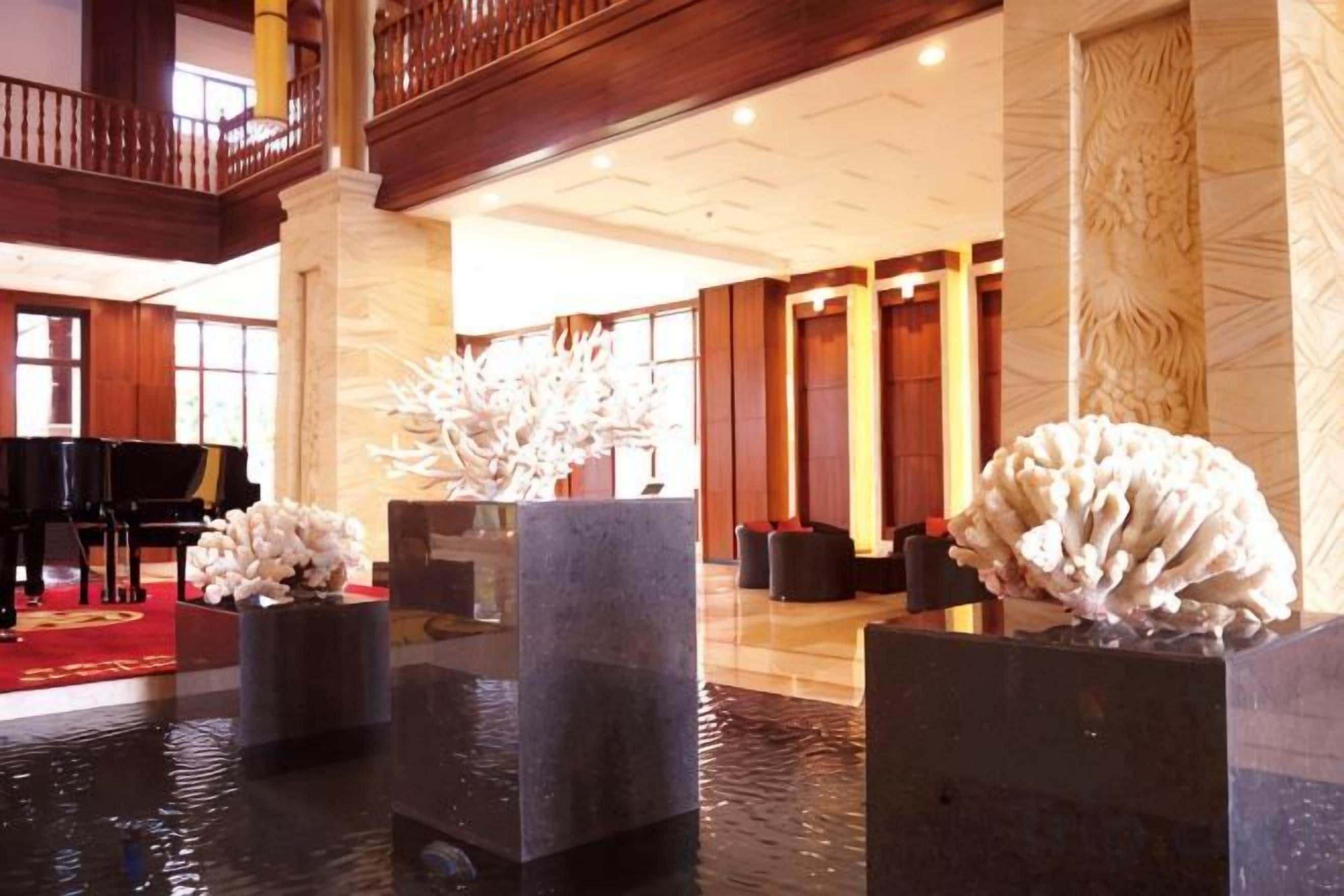 Een lobby met een vleugel, een fontein met witte sculpturen en een hoog plafond met een balkon.