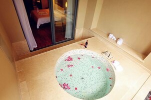 A bathroom with a large bathtub, a glass door leading to a bedroom, and a small shelf with toiletries.