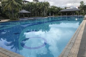 Ein klares Schwimmbecken mit einer gefliesten Kante, umgeben von Palmen und einem Gazebogebäude.