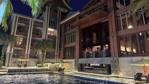 Un hotel con zona de piscina, asientos al aire libre y una fachada bien iluminada de noche.