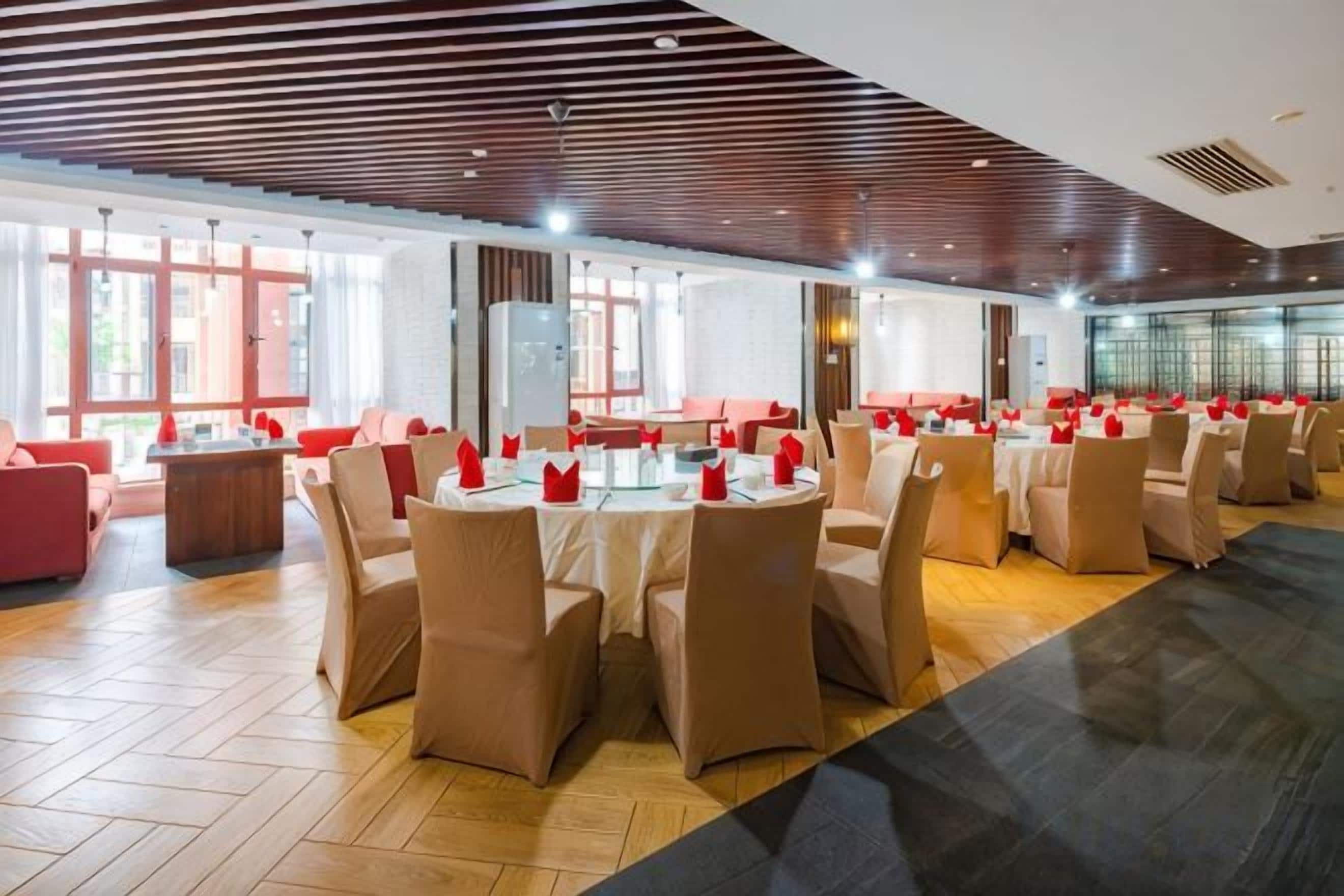 A spacious dining area with round tables and chairs, large windows, and a modern ceiling design.