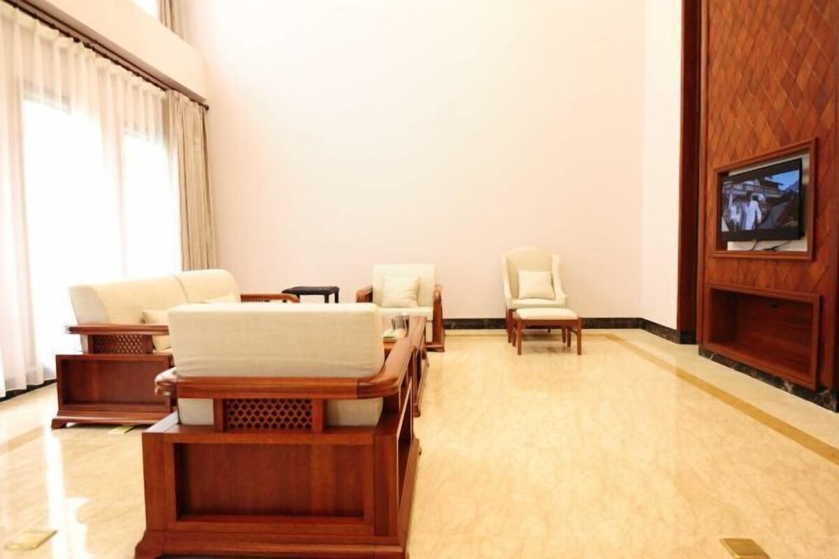 A hotel lobby with a wooden sofa set, a television mounted on the wall, and a large window with curtains.