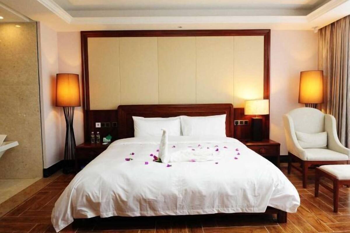 A hotel room with a large bed, two bedside lamps, a chair, and a nightstand with a lamp.