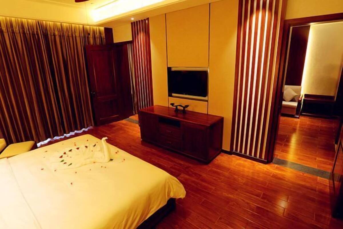 A hotel room with a bed, a TV, a wooden dresser, and a curtain.