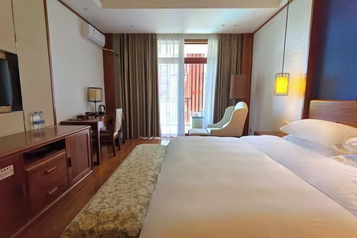 A hotel room with a bed, a desk, a chair, a TV, and a window with curtains.