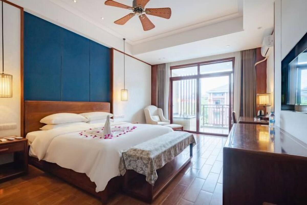 A hotel room with a large bed, a desk, a chair, and a balcony with a view.