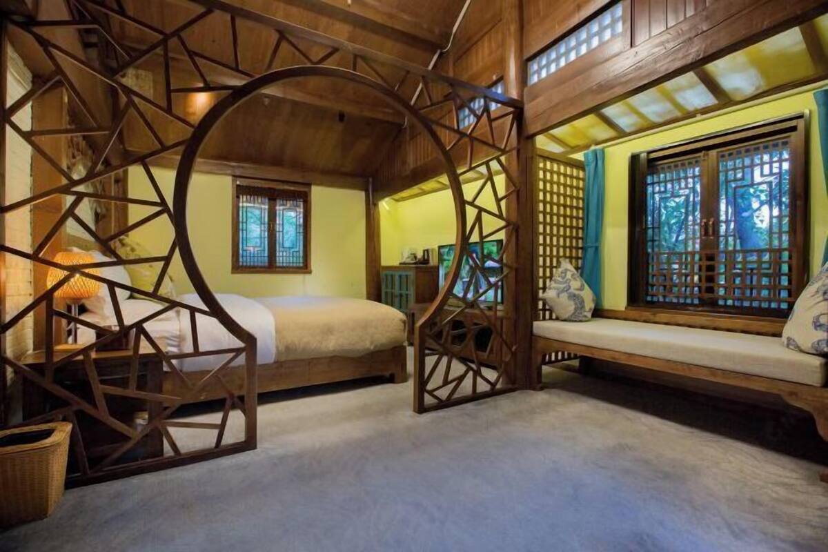 A traditional room with a bed, a wooden bench, and a window with a lattice design.