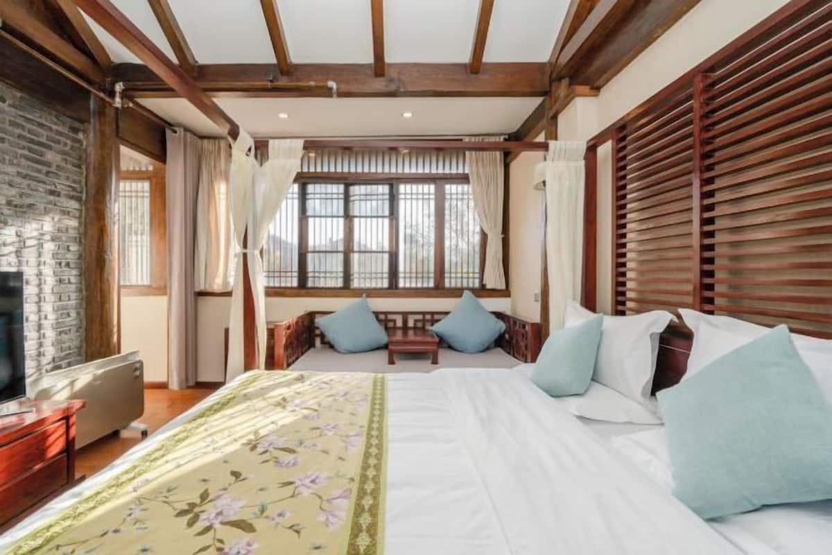 A bedroom with a large bed, wooden beams, a stone wall, and a window with curtains.