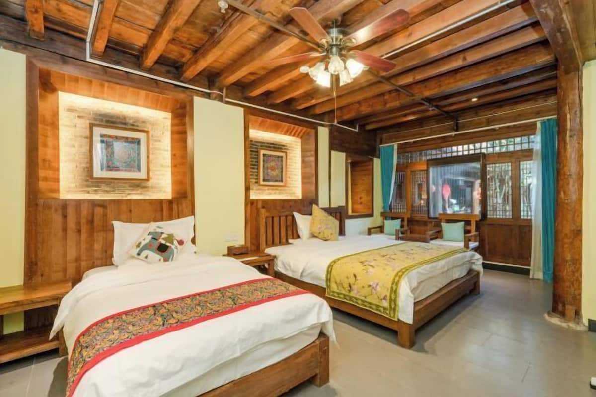 A room with two wooden beds, a ceiling fan, and a window with curtains.