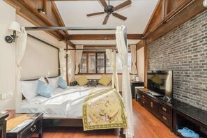 Una habitació amb un llit, televisió, paret de maó i ventilador de sostre.