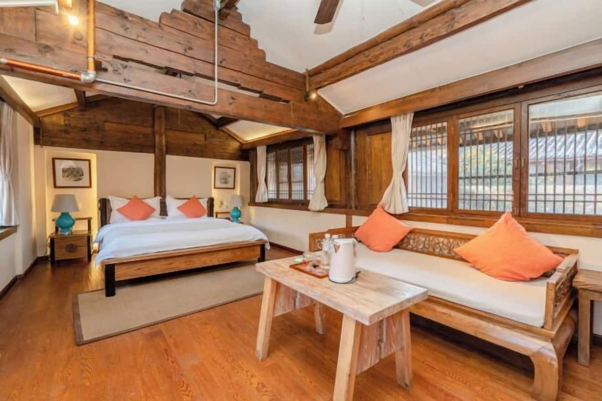A cozy room with wooden beams, a bed, a sofa, and a table with a kettle.