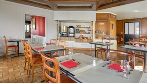 Een restaurant met houten tafels en stoelen, een keukenhoek en een rode accentmuur.