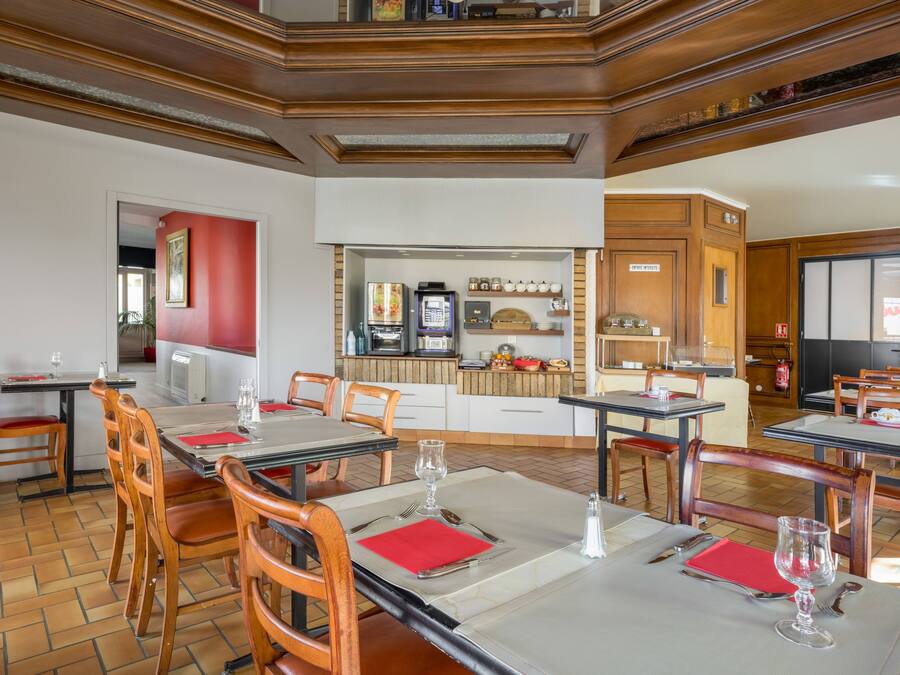 A restaurant with wooden tables and chairs, a kitchen area, and a red accent wall.