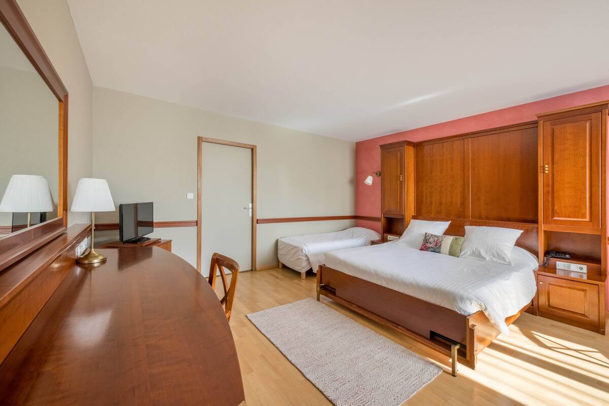 Une chambre à coucher comprenant un lit, des tables de chevet, un bureau, une chaise, une télévision et un miroir.