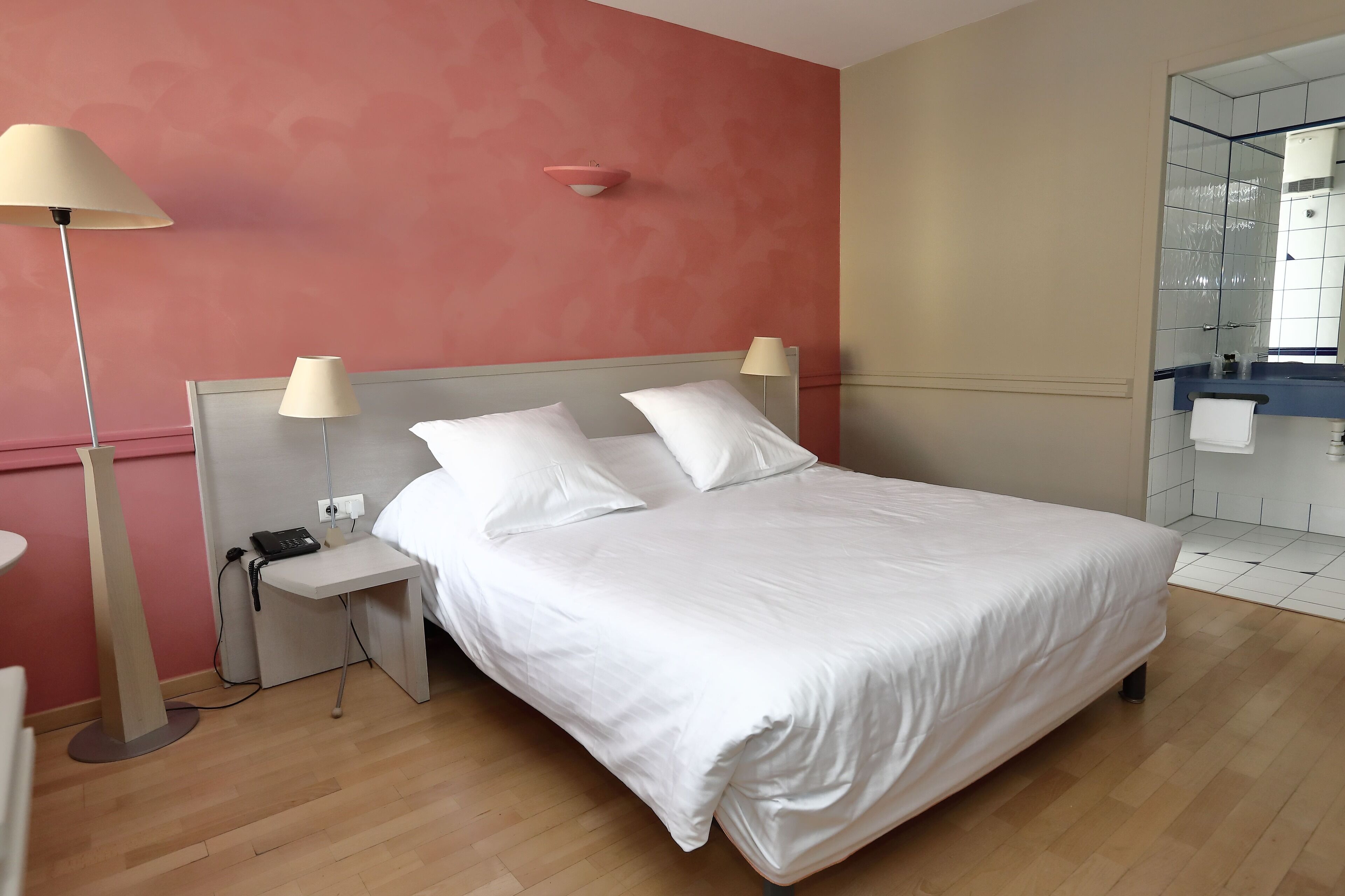 A hotel room with a bed, bedside lamps, a nightstand, and a mirror.