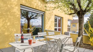 Een terras buiten met witte metalen tafels en stoelen, een Coca-Cola fles en een glas rode drank.