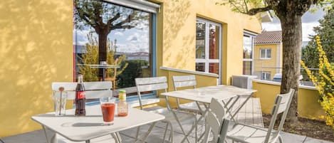 An outdoor patio with white metal tables and chairs, a bottle of Coca-Cola, and a glass of red drink.