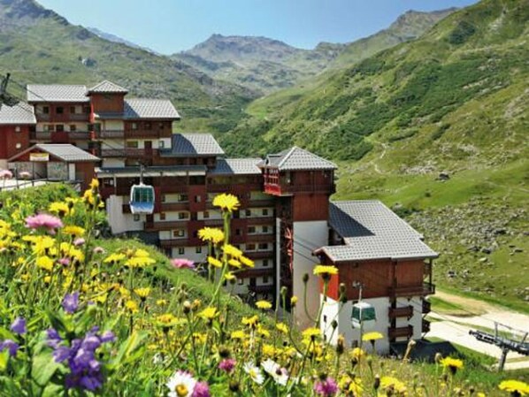 Traditional chalet-style hotel with a symmetrical facade and sloped roof, set amidst lush greenery and wildflowers.