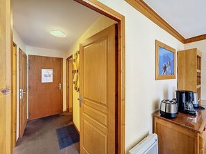 Um corredor de hotel com portas de madeira, um radiador, uma cafeteira e um quadro na parede.
