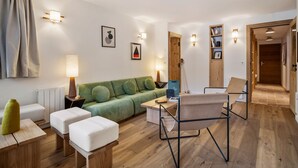 Ein modernes Wohnzimmer mit einem grünen Sofa, weißen Hocker, einem Stuhl mit Metallgestell und einem Couchtisch aus Holz.