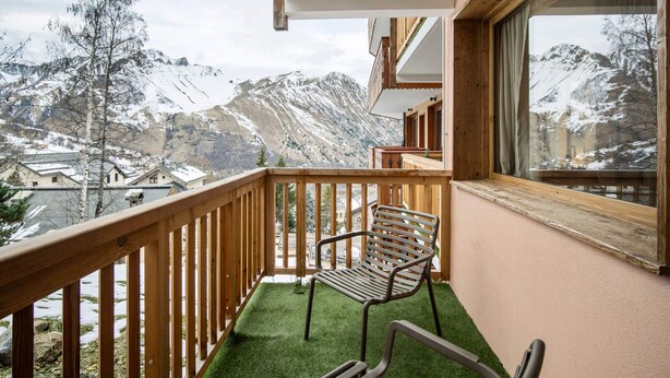 Ein Balkon mit Holzwertung, einem Metallstuhl und Blick auf schneebedeckte Berge.
