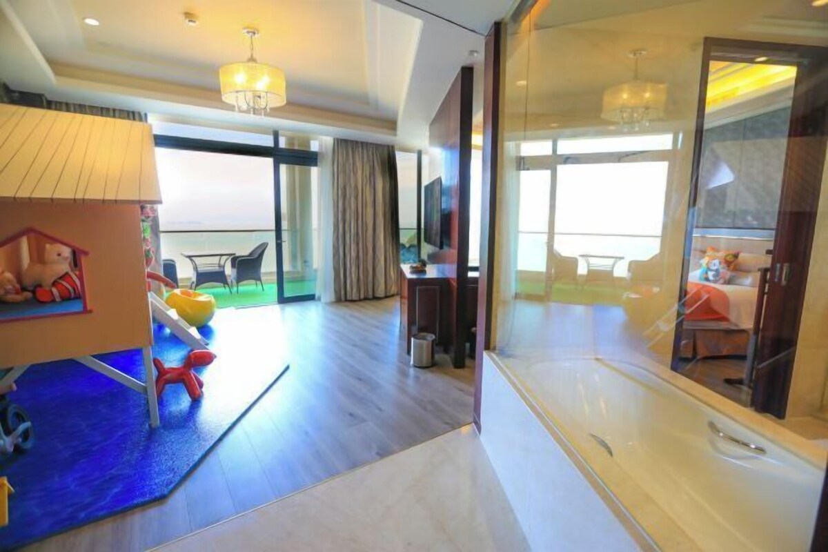 A hotel room with a balcony, a play area, a dining area, and a large window.