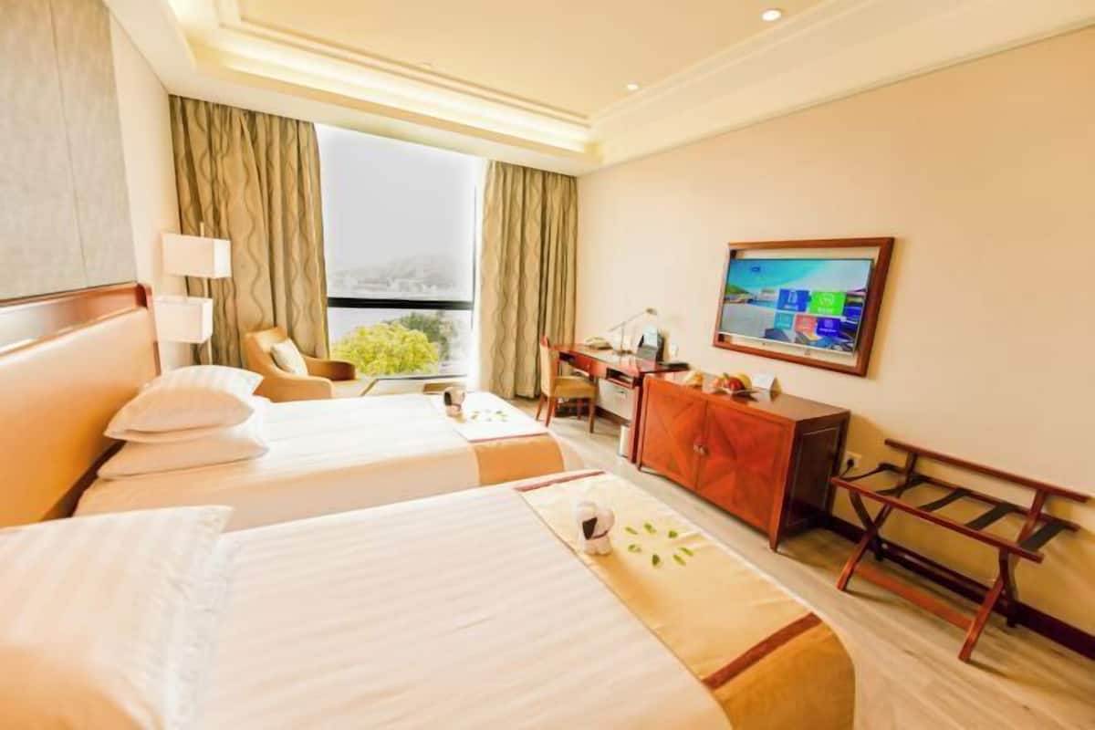 A hotel room with two beds, a desk, a chair, a television, and a view of the outdoors.