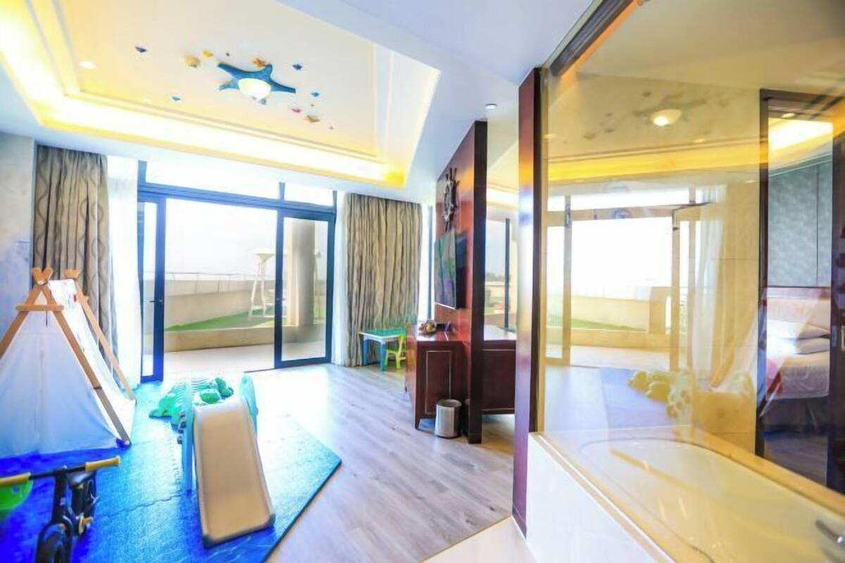 A modern hotel room with a large sliding glass door, a desk, a chair, a small table, and a tent-like structure.