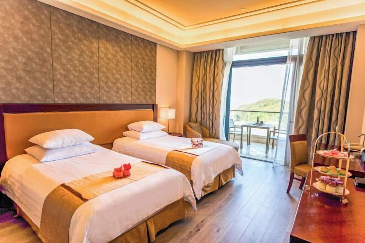 A hotel room with two beds, a dining table with a three-tiered dessert cart, and a balcony with a view.