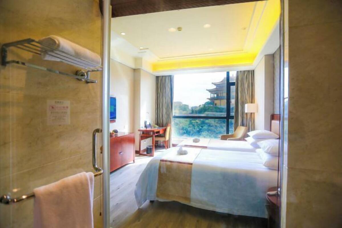 A hotel room with a bed, a desk, a chair, and a view of a traditional building.