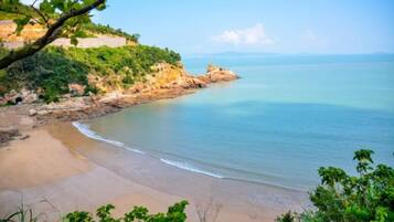 A coastal landscape with a beach, greenery, and a clear sky.
