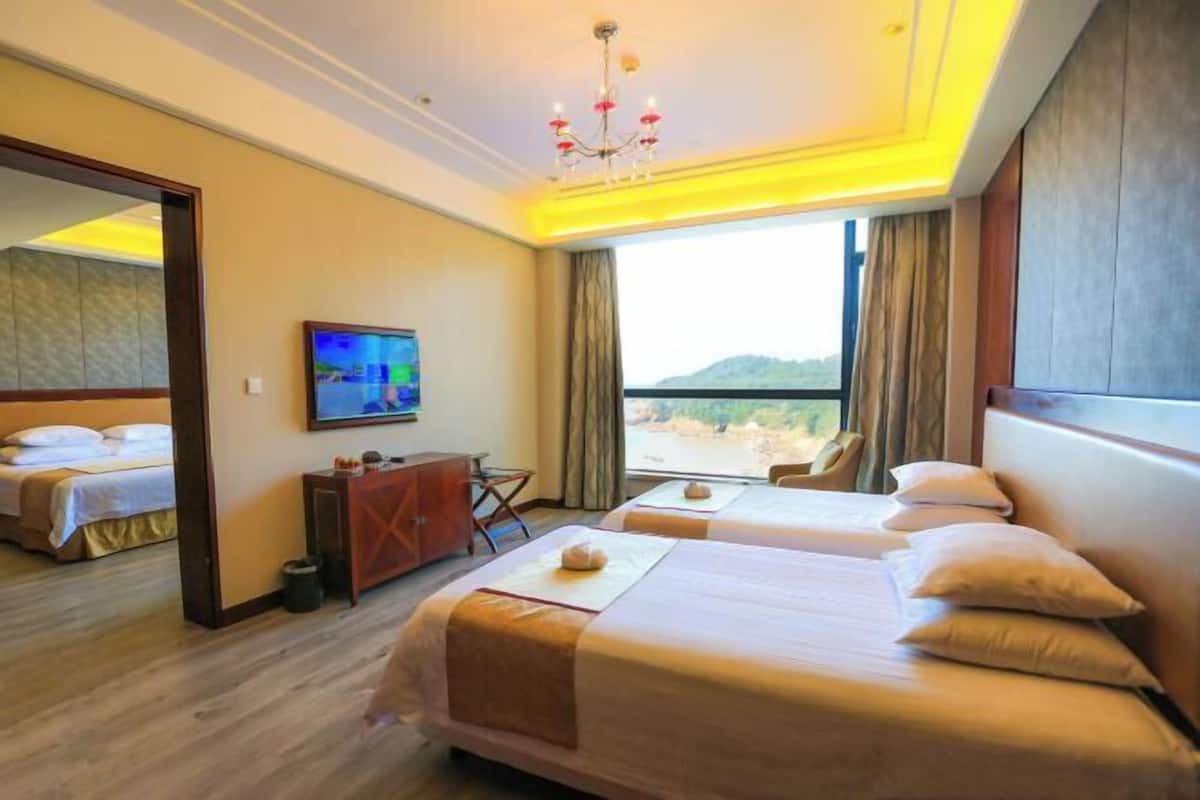 A hotel room with two beds, a TV, a desk, and a view of the outdoors.